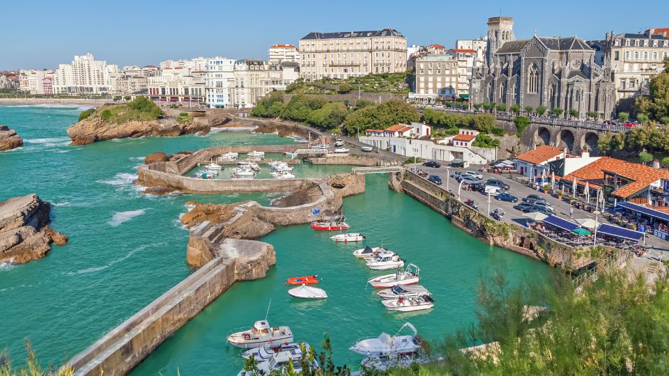 Vue du Port des Pêcheurs à Biarritz avec des bateaux amarrés et l'église Sainte-Eugénie en arrière-plan, entourée de bâtiments pittoresques.