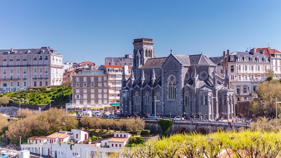 Église Sainte-Eugénie à Biarritz, entourée de bâtiments résidentiels et d'arbustes, sous un ciel bleu éclatant.